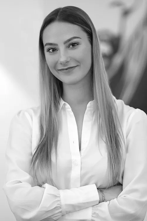 Julia Petermann, Teammitglied bei KITICON Global Networks in weißem Hemd vor verschwommenem Hintergrund mit verschränkten Armen, schwarz-weißes Bild.